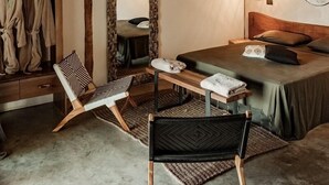 Ein rustikales Schlafzimmer mit einem Strohdach, einem Bett mit Holz Kopfteil, einer Hängeleuchte und einem Spiegel an der Wand.
