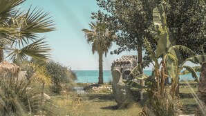 Ein tropischer Garten mit einer Steinstruktur, Palmen und Blick auf das Meer.