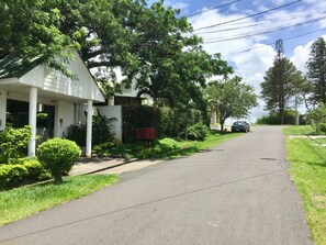 A residential street with houses, greenery, and a parked car. - Serenitas (San Rafael)