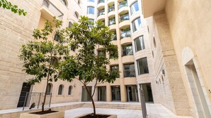 A courtyard with two trees in planters, surrounded by a multi-story building with balconies. - Amazing 2 Bedrooms/Gym/Parking in city center (Jerusalem)