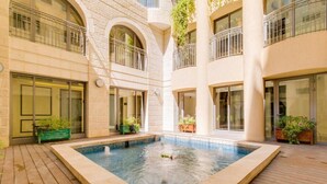 A courtyard with a swimming pool, wooden deck, and potted plants. - Amazing 2 Bedrooms/Gym/Parking in city center (Jerusalem)