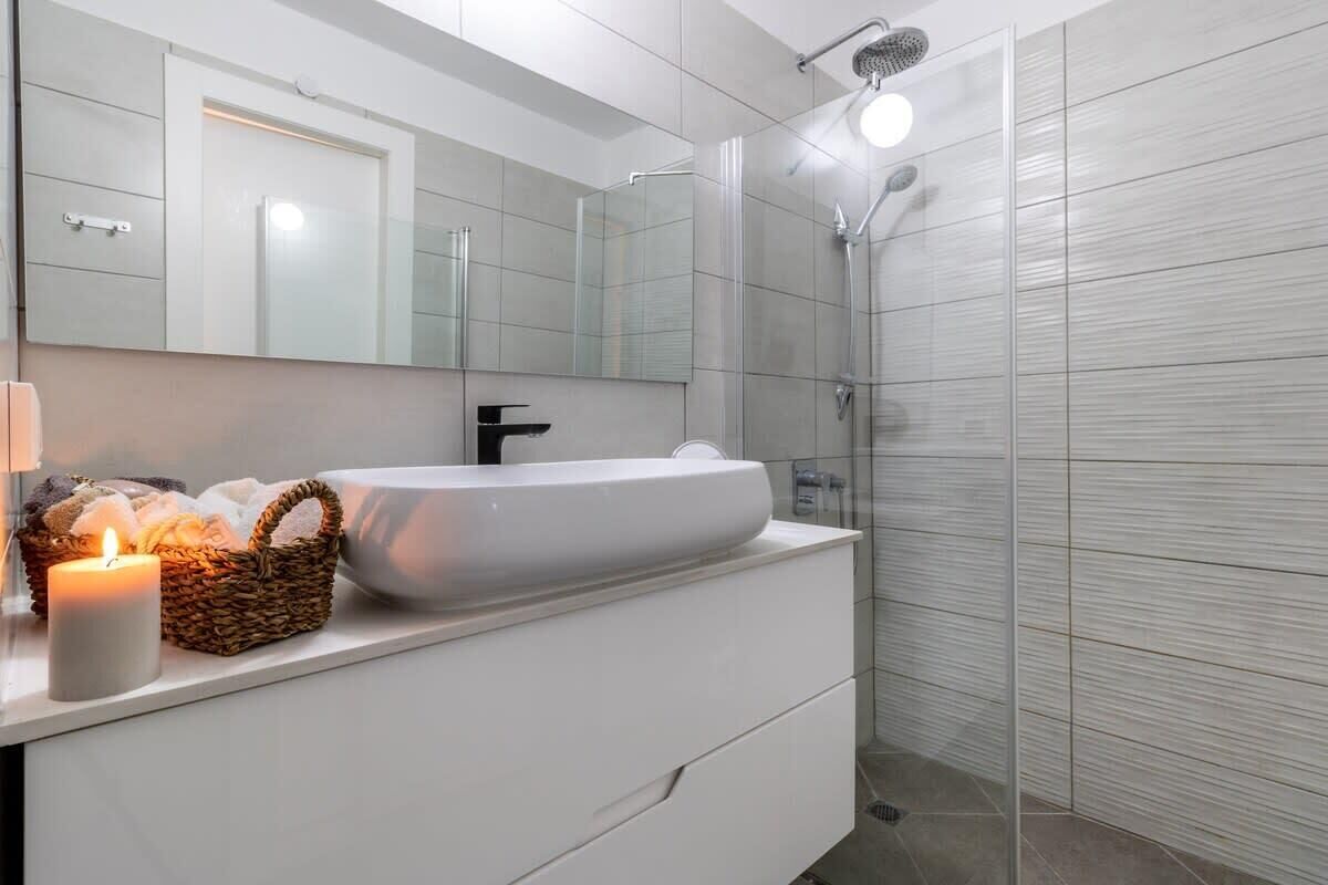 Un baño moderno con un lavabo blanco grande, un espejo y una zona de ducha.