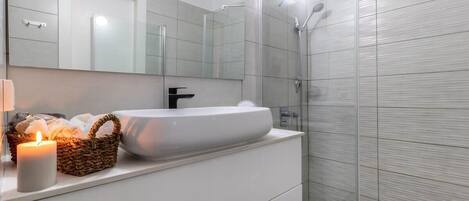 Un baño moderno con un lavabo blanco grande, un espejo y una zona de ducha.