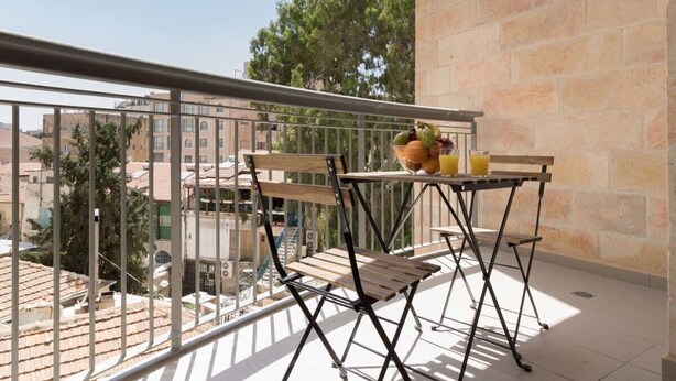 A balcony with a table and chairs, a potted plant, and a view of buildings and trees. - Beautiful appartment in city center (Jerusalem)