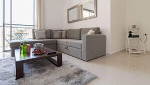 A modern living room with a grey sectional sofa, a coffee table with snacks, a large mirror, and a white ladder against the wall. - Beautiful appartment in city center (Jerusalem)