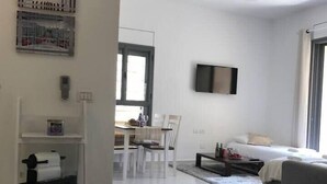 A modern hotel room with a bed, a TV, a dining area with chairs, and a kitchen area with a fridge. - Beautiful appartment in city center (Jerusalem)