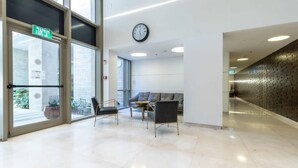 A modern lobby with a glass door entrance, a clock, and a seating area with a sofa and chairs.