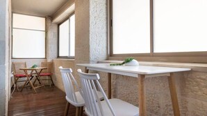 A small, cozy room with a wooden floor, white chairs, a white table, and a large window providing natural light.