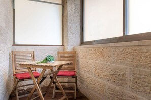 A corner room with a wooden table and two chairs, a green plant on the table, and a stone wall. - Haneviim Court Complex - 1 Bedroom (Multi-unit) (Jerusalem)