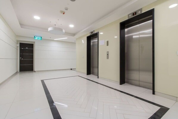 A modern elevator area with two elevators, a digital display, and a clean, tiled floor.