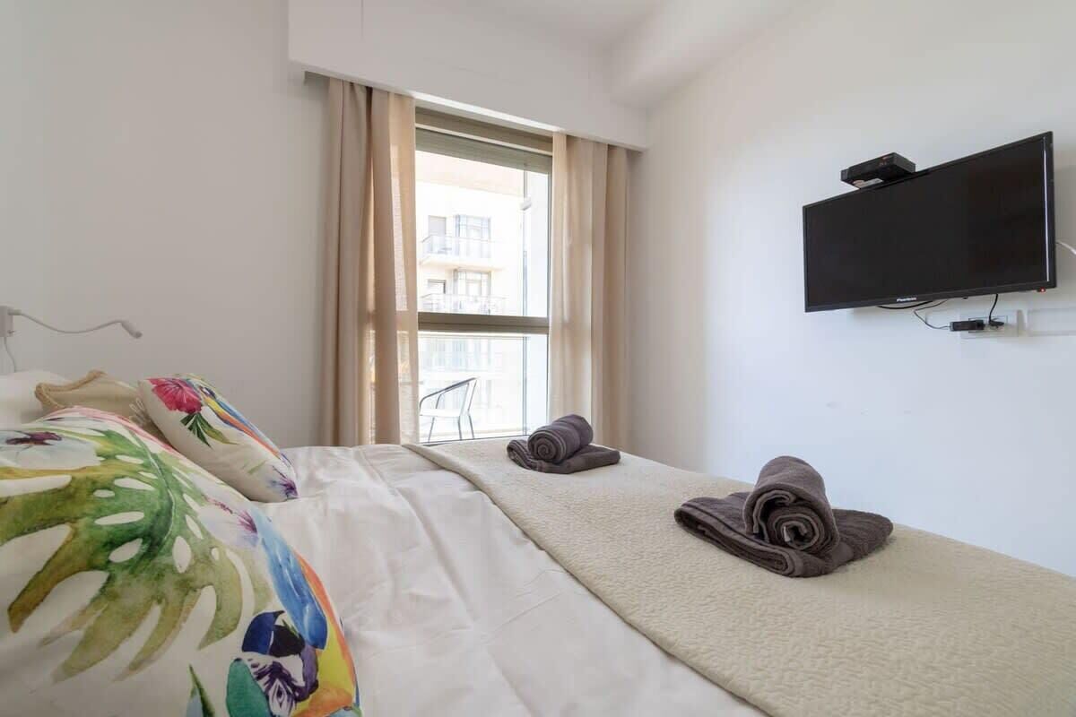 Une chambre d’hôtel avec un lit, un téléviseur fixé au mur et une fenêtre avec des rideaux.