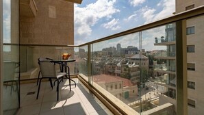 A balcony with a table and chairs, a glass railing, and a city view.