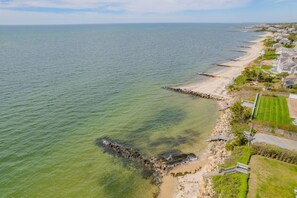 Vista aerea di una zona costiera con spiaggia ampia e chiara, un litorale roccioso e edifici residenziali lungo la riva.