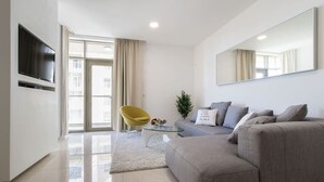 A modern living room with a grey sofa, a yellow chair, a small coffee table, and a flat-screen TV mounted on the wall.