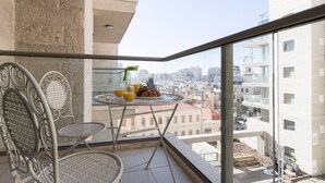 A balcony with a table set for breakfast, a chair, and a view of the cityscape.