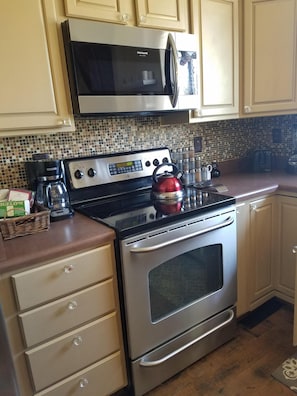 Fully equipped kitchen with stainless steel stove, microwave, and kettle, perfect for preparing meals.