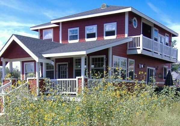 Stunning two-story home with a charming front porch and balcony, set amidst a beautiful garden with vibrant sunflowers.