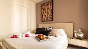 Una cama bien hecha con una bandeja de pasteles y flores, una mesita de noche con una lámpara y una obra de arte en la pared.