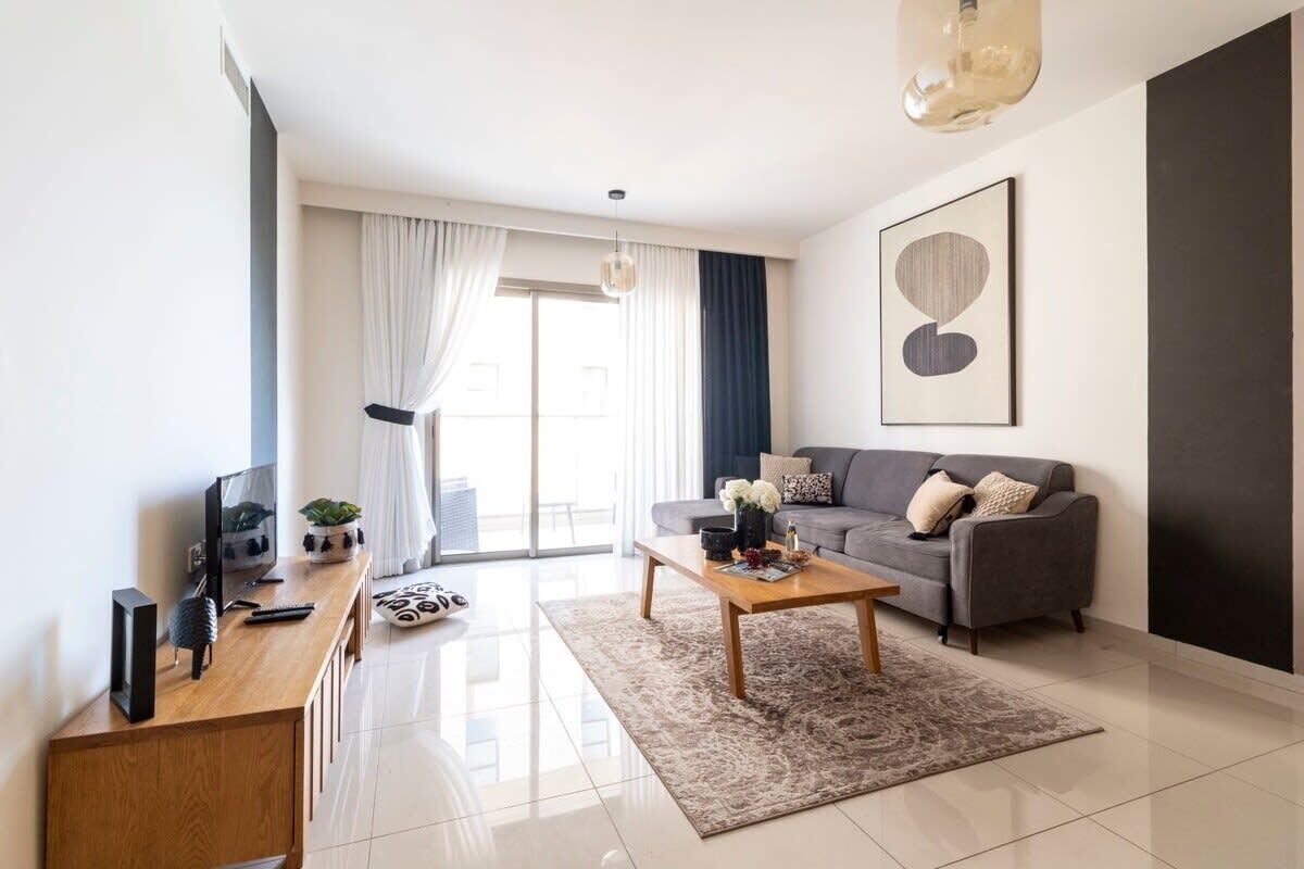 Una sala de estar moderna con un sofá gris, una mesa de centro de madera y un televisor sobre un mueble bajo de madera.
