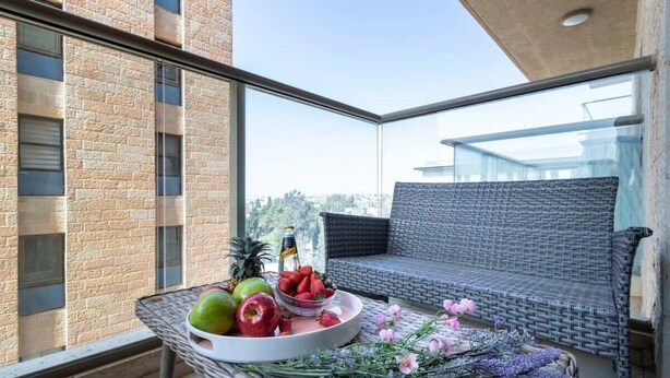 Un balcón con mobiliario de mimbre, una bandeja de frutas y flores, y vistas a la ciudad.