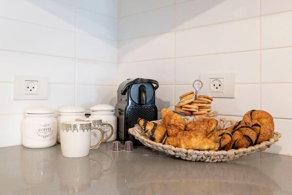 Una encimera de cocina con tazas de café, una cafetera y un cesto de croissants.