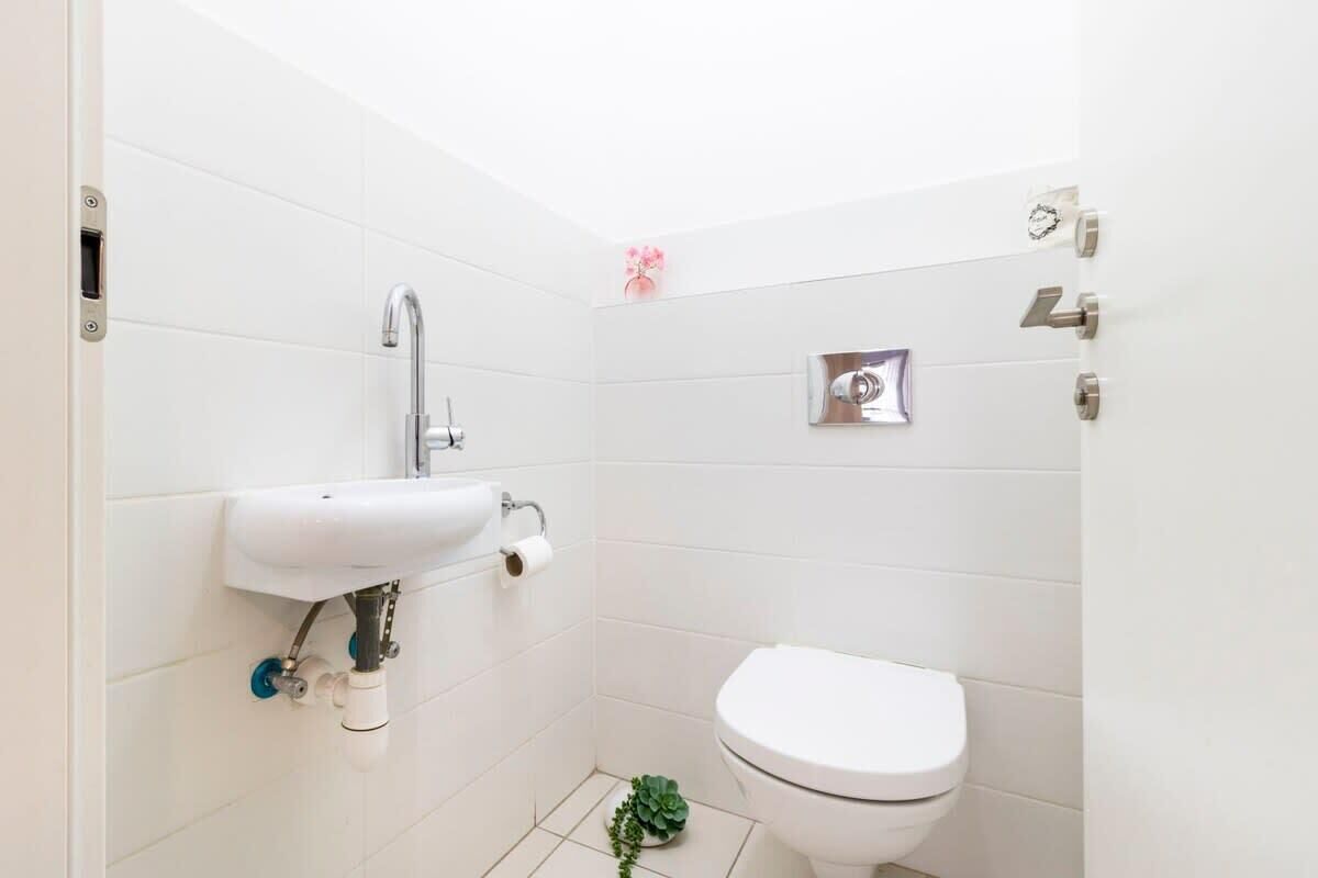 Een kleine, schone badkamer met witte tegels, een witte wastafel, toilet en een kleine plant.