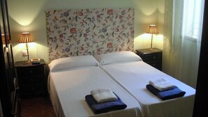 Habitación doble con dos camas, papel tapiz floral, lámparas de noche y un ventanal con cortinas de gasa.