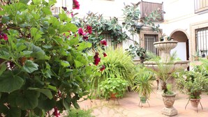 Un patio con plantas en macetas, una fuente de piedra y un piso de baldosas.