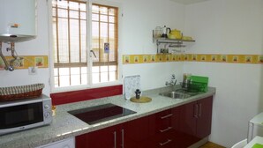 Una cocina con microondas, lavamanos y armarios rojos.