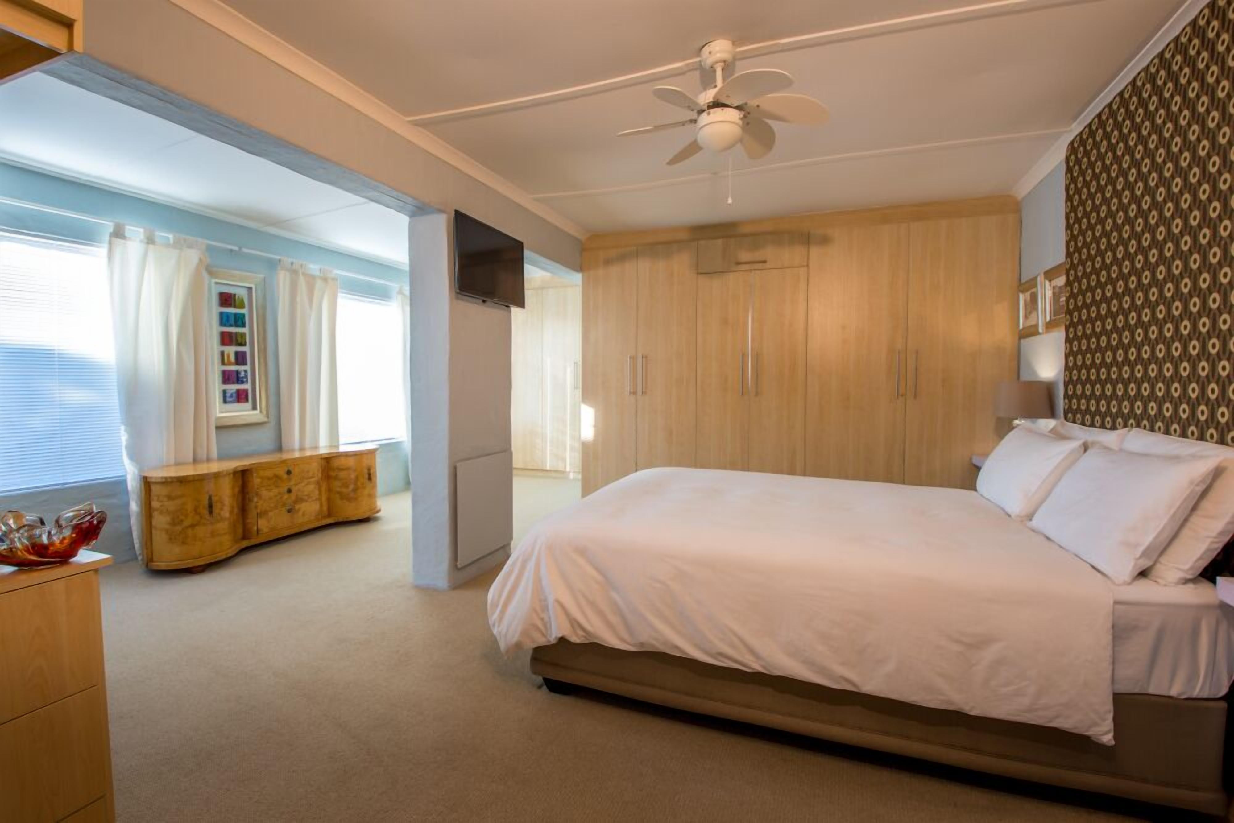 Ein Schlafzimmer mit einem Bett, einem Deckenventilator, einem Holzschrank und einem Fenster mit Vorhängen.