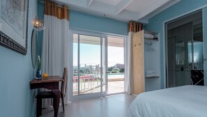 Un dormitorio con una cama, un escritorio con silla, un ventanal con cortinas y una puerta corrediza de vidrio que da a un balcón.