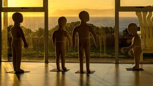 Cuatro figuras infantiles de pie sobre esteras en una habitación con amplios ventanales que dan a una vista panorámica.