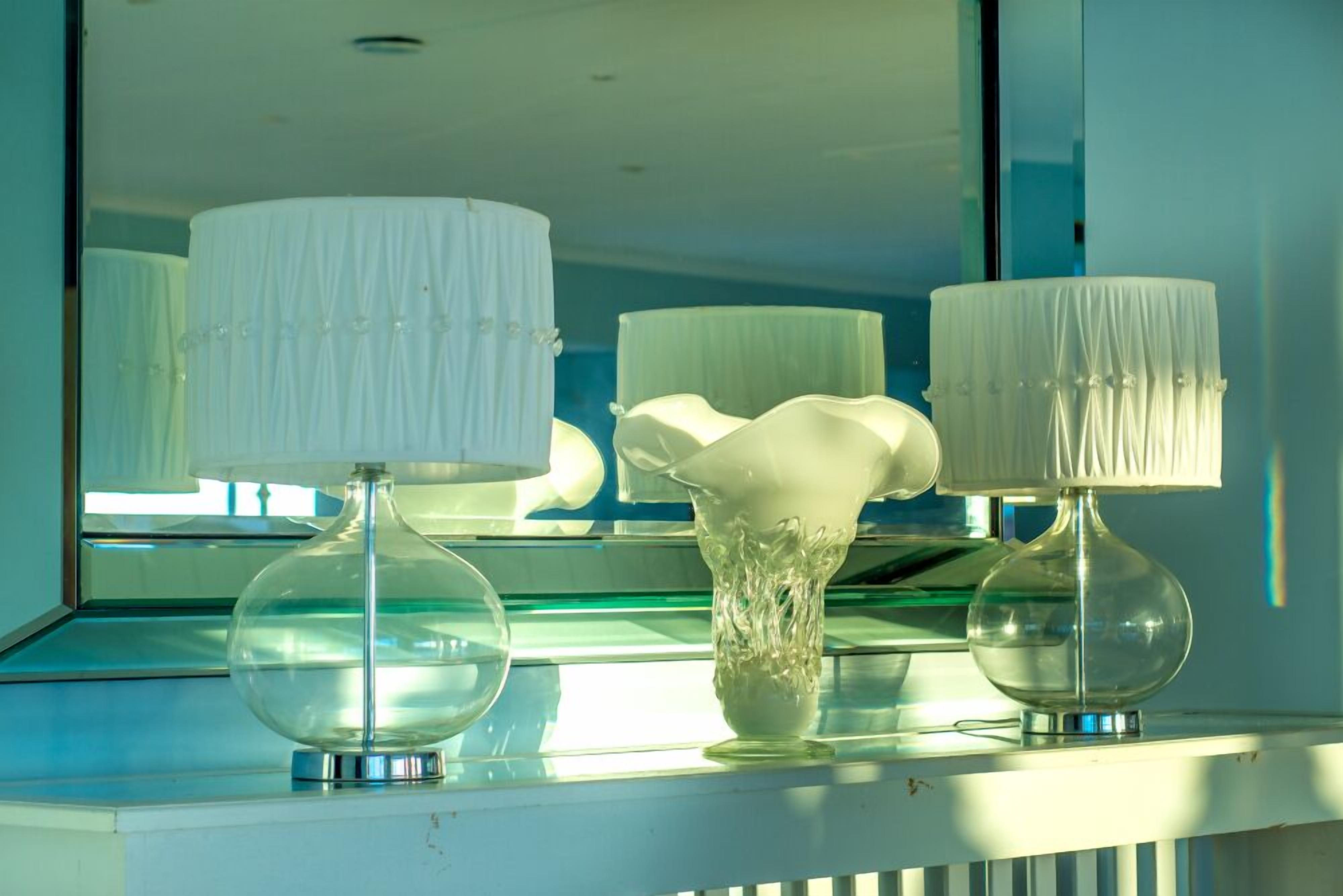 A room with a large mirror reflecting two lamps and a vase.