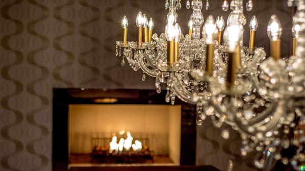 Un candelabro con múltiples luces y una chimenea al fondo.