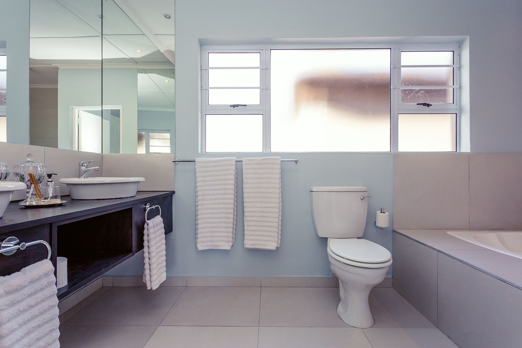 Een moderne badkamer met toilet, wastafel en bad. Twee handdoeken hangen aan een rek, en boven de wastafel hangt een grote spiegel.