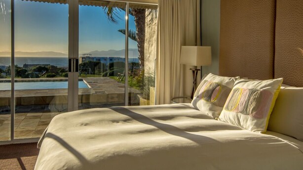 Habitación de hotel con una cama grande, vista a una piscina y montañas, y una puerta corrediza de vidrio.