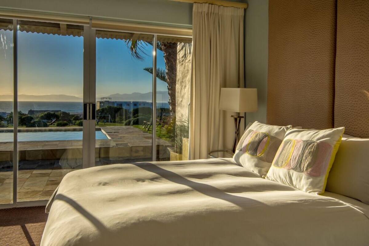 A hotel room with a large bed, a view of a pool and mountains, and a sliding glass door.