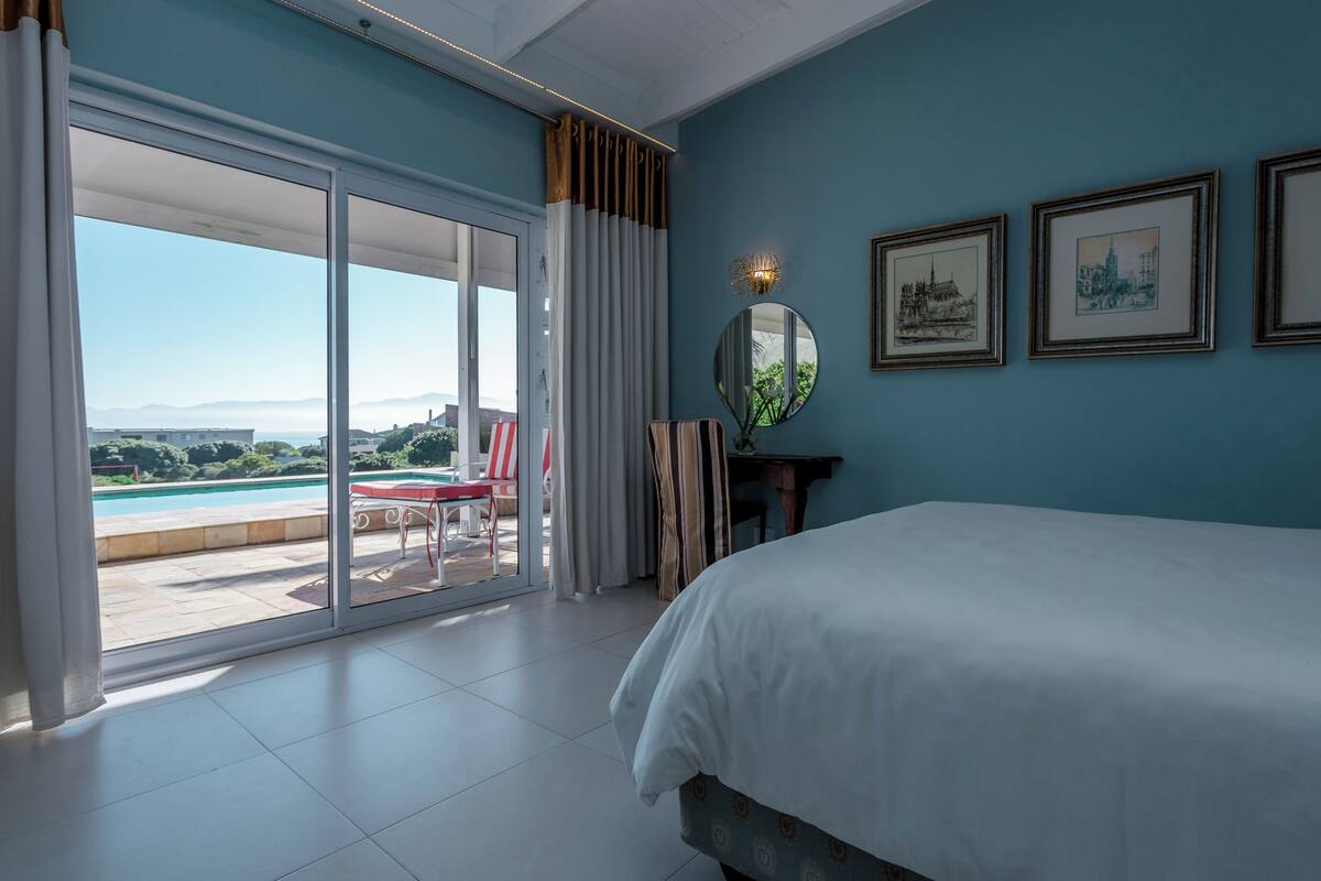 A bedroom with a large bed, a view of a swimming pool, and a balcony with a chair.
