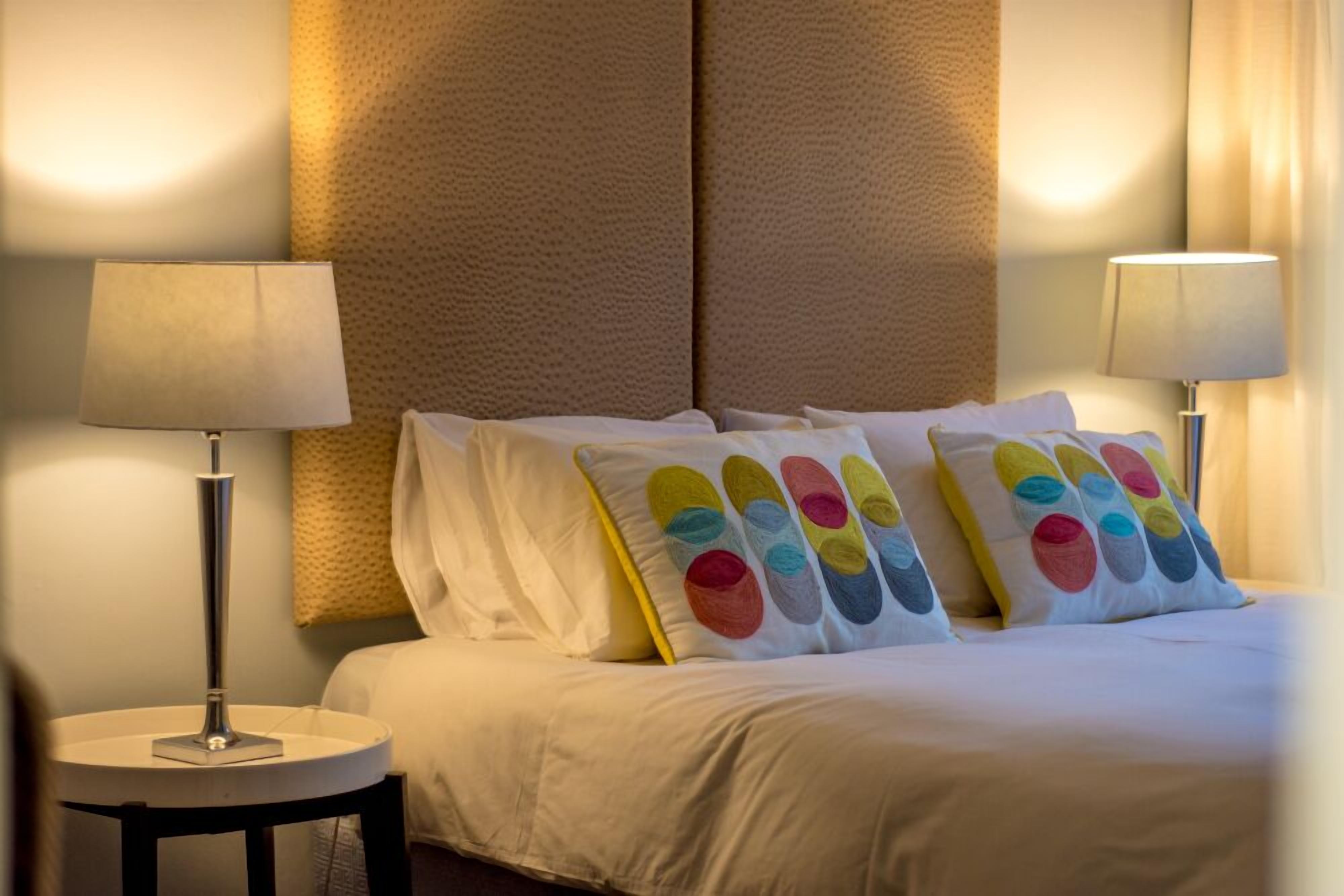 Una camera d'albergo con un letto, due lampade ai comodini e una parete decorata.
