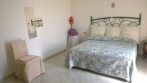 Une chambre à coucher avec un lit, une chaise et une petite table sur laquelle est posé un vase de fleurs.