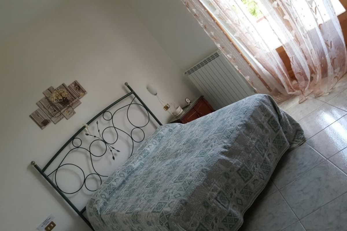 A bedroom with a metal bed frame, patterned bedspread, and a radiator.