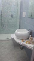 Un baño con lavamanos blanco, un espejo y zona de ducha.