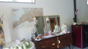 Une pièce comprenant une commode en bois, un grand miroir, une carte accrochée au mur, ainsi que divers objets décoratifs, notamment un vase avec des fleurs et une petite table sur laquelle sont posées des théières.