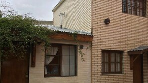 Un bâtiment à deux étages avec une façade en briques, une porte en bois et une fenêtre avec des rideaux. Des plantes en pot sont disposées au sol.