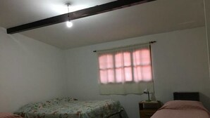 Une petite pièce faiblement éclairée, avec un lit simple, une table de chevet et une fenêtre avec des rideaux.