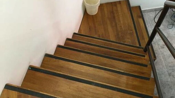 Un escalier en bois avec des marches à bords noirs, un mur blanc et un plancher gris.