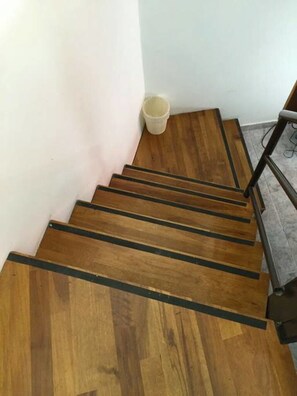 A wooden staircase with black edges, a white wall, and a grey floor.