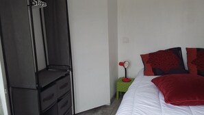 A bedroom with a bed, a nightstand, a red fan, and a wardrobe. - 2 minutes walk from the beach (Pornic)