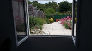 A view through a window of a garden with a paved path, a wooden fence, and various plants and flowers. - 2 minutes walk from the beach (Pornic)