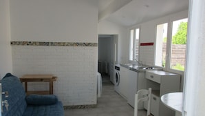 A compact kitchen with a washing machine, a small table, and a blue sofa. - 2 minutes walk from the beach (Pornic)
